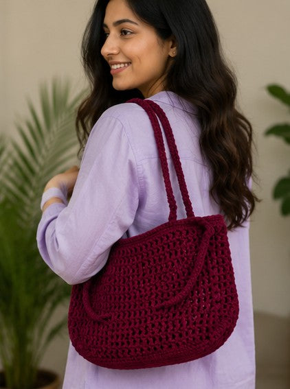 Woman carrying Handmade burgundy crochet shoulder bag with minimalist woven design for everyday use.